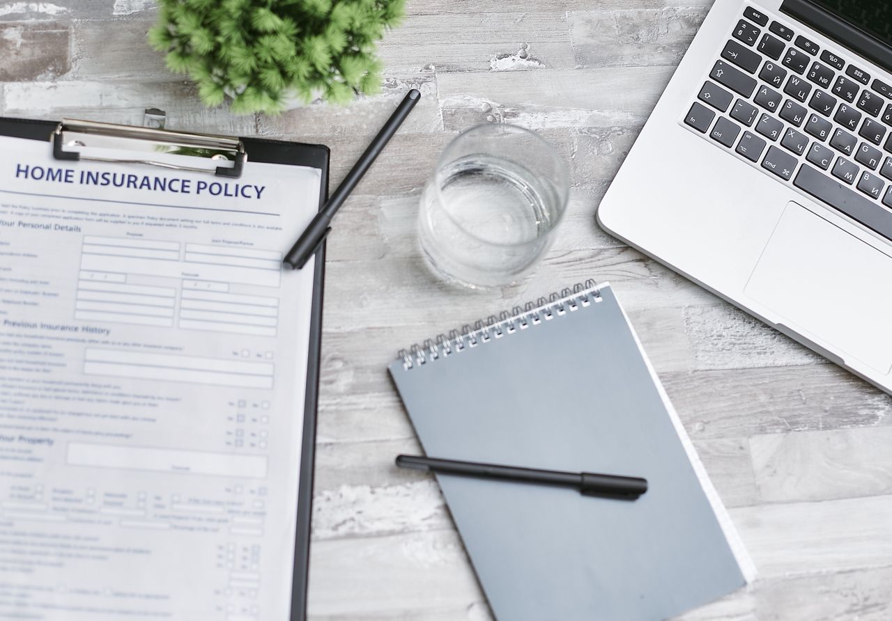 Flat lay of a workspace with a home insurance policy, laptop, and notebook on a desk.